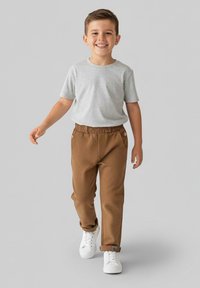 Dziecko w jasnoszarej koszulce i brązowych spodniach z elastycznym paskiem, do tego białe trampki. Strój jest casualowy i wygodny.