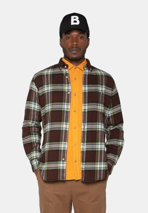 Chemise en flanelle à carreaux marron avec des accents verts et bleus sur une chemise à boutons orange vif. Casquette noire avec un logo 'B' blanc.