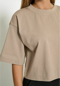 Beige cropped t-shirt made of soft cotton, featuring a round neckline and short sleeves with a loose fit and minimal stitching details.