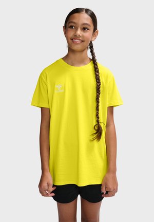 Lys gul bomulds T-shirt med afslappet pasform, korte ærmer og et lille hvidt logo på venstre bryst. Båret med sorte shorts.