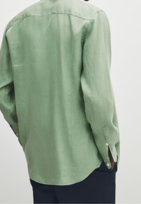 Ljusgrön linneskjorta med lång ärm och rundad nederkant. Har knäppta manschetter och en bakre okdesign för extra struktur.