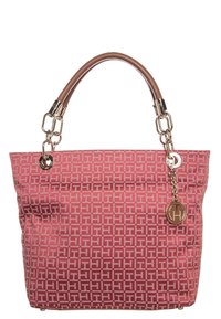 Sac à main à motifs rouges avec des poignées en cuir beige, des maillons en chaîne dorés et un charme rond en or portant les initiales "TH."