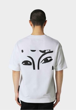 Weißes Baumwoll-T-Shirt mit einem großen schwarzen grafischen Design stilisierter Augen auf der Rückseite. Kurze Ärmel mit lockerer Passform.