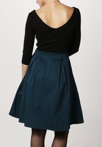 Top negro de manga larga con un escote en V profundo; combinado con una falda A-line de color teal con pliegues y una textura suave.