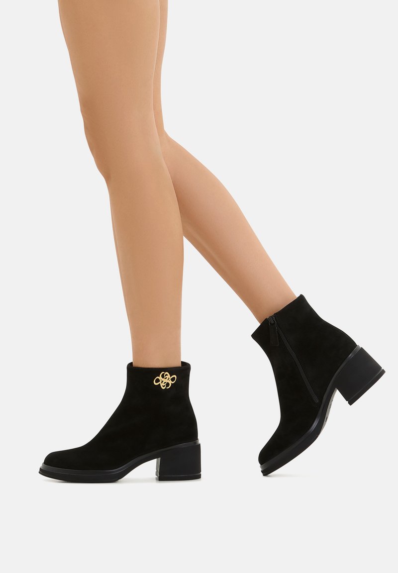 Stivali alla caviglia in suede nero con tacco quadrato, dotati di un dettaglio decorativo in oro e zip laterale. Texture liscia e design elegante.