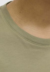 Camiseta de cuello redondo en color verde oliva con una textura suave, que presenta un cuello acanalado y costuras visibles a lo largo del escote.