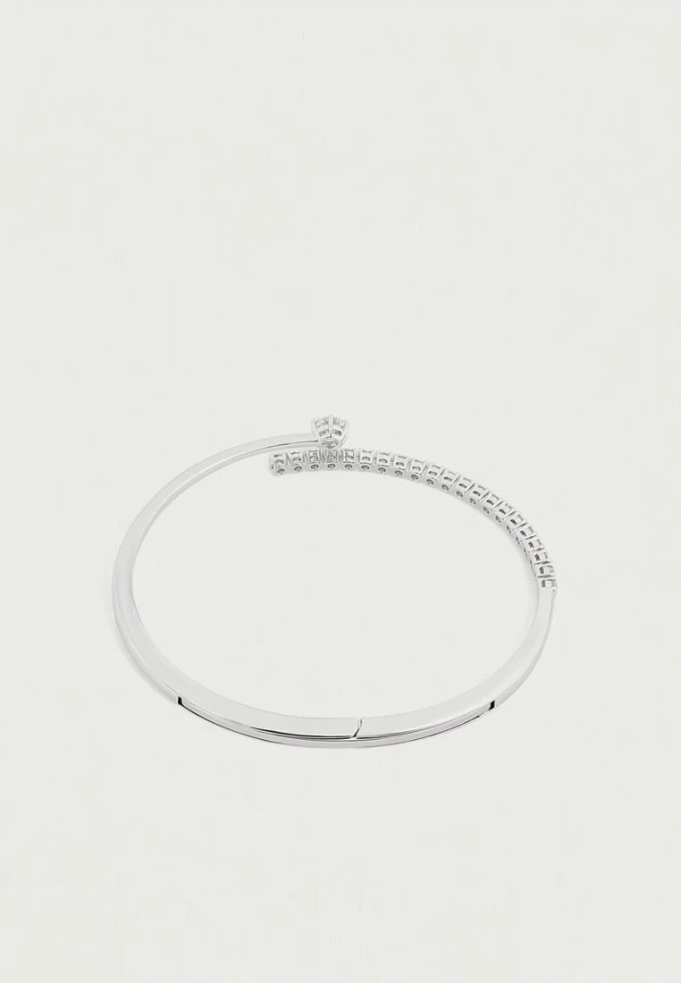 Un bracelet jonc argenté à charnière, orné d’une rangée de petites pierres transparentes sur un côté, présenté sur un fond blanc uni.