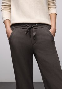 Dunkelgraue Jogginghosen mit Seitentaschen, elastischem Bund und verstellbarem Kordelzug. Glatt strukturierter Stoff mit entspannter Passform.