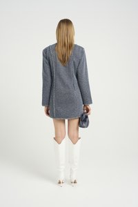 Tweed mini-kåpe i blågrå med teksturert overflate, lange ermer og frynset kant. Kombinert med hvite knehøye støvler og en liten svart veske.