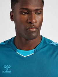 Teal sports trøje med v-hals, lyseblå accenter på skuldrene og hvid kant. Har et logo på venstre brystområde.