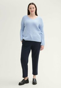 Jasnoniebieski sweter z dzianiny z dekoltem w serek i wzorem w zygzak, zestawiony z granatowymi spodniami o wąskim kroju i czarnymi butami na grubej podeszwie.
