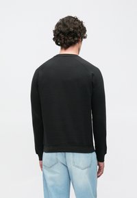 Sweatshirt noir à manches longues avec poignets et ourlet côtelés, doté d'un col rond et d'une coupe décontractée, associé à un jean bleu clair.