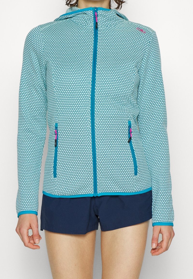 Giacca con cappuccio e zip di colore blu chiaro con un motivo esagonale. Presenta due tasche frontali con zip e accenti di blu scuro in contrasto.