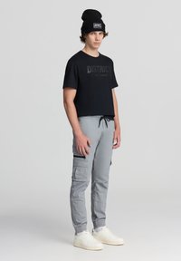 Czarna koszulka z krótkim rękawem z nadrukiem "DISTRICT" w kolorze czarnym, w połączeniu z jasnoszarymi spodniami cargo z bocznymi kieszeniami i elastycznymi mankietami. Białe sneakersy.