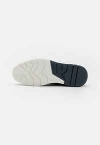 Semelle de chaussure avec un dessus en caoutchouc bleu foncé durable et une semelle blanche avec un motif en zigzag pour l'adhérence.