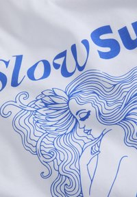 Bílá látka s modrým liniovým uměním ženy s vlnitými vlasy, prsty se dotýká brady, doplněno textem "Slow Sur."
