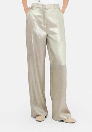 Metallic silver wide-leg trousers with a smooth texture, high waist, and side pockets, paired with light beige slip-on shoes.
