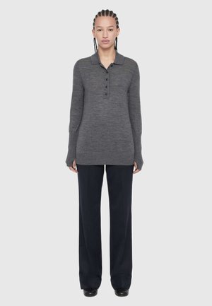 Young person with braided hair wearing a long-sleeve gray buttoned polo sweater and black wide-leg pants, standing against a plain background.