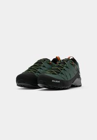 Sapatos de caminhada verdes e pretos com um cabedal em malha texturizada, ponta reforçada e atacadores em contraste com um logótipo da marca incorporado.