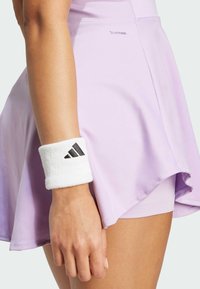 Light purple performance skirt with a flared design, featuring a white absorbent wristband with black logo accents. Smooth fabric texture.