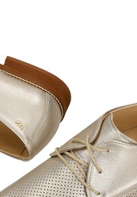 Metalen zilveren leren veter schoenen met geperforeerd teenontwerp en bruine rubberen zolen, weergegeven in een close-up weergave.