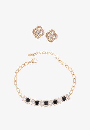 Brățară de aur cu pietre prețioase negre și transparente alternative, asortată cu cercei tip stud din aur împodobiți cu pietre transparente.