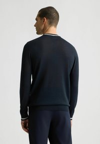 Suéter de punto azul marino con mangas largas, cuello redondo y acentos de rayas en contraste en el cuello y los puños. Material texturizado.