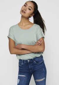 Hellgrünes Kurzarm-T-Shirt mit Rundhalsausschnitt, kombiniert mit dunkelblauen Jeans aus Denim mit rissigen Akzenten und einer taillierten Passform.