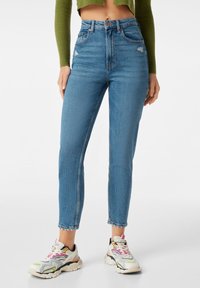 Blå högmidjade skinny jeans med lätt slitning, denimtyg, ankle-length skärning, ihopparat med flerfärgade sportskor.