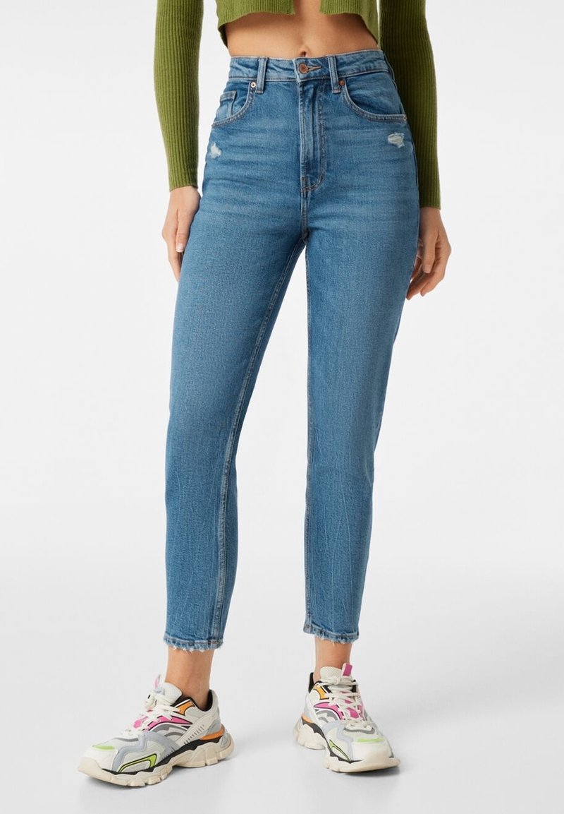 Blå högmidjade skinny jeans med lätt slitning, denimtyg, ankle-length skärning, ihopparat med flerfärgade sportskor.