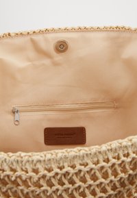 Intérieur de sac tissé beige avec une doublure en tissu lisse, une poche zippée et une étiquette en cuir. Conception à ouverture supérieure avec une texture naturelle.