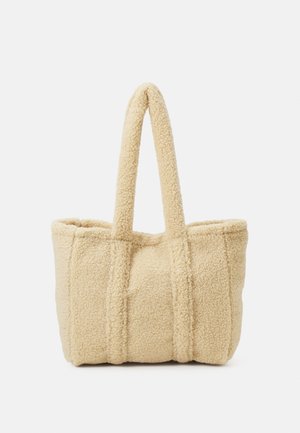 Sac fourre-tout beige en polaire avec une texture douce et deux bretelles, debout sur un fond uni clair.