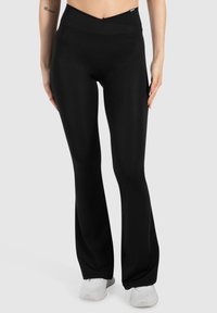 Zwarte flared legging gemaakt van rekbaar materiaal met een hoge tailleband, met een gladde textuur en minimale details op de tailleband.