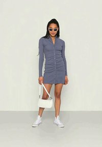 Vestido de mangas longas com botões em azul ardósia, com um design franzido, combinado com acessórios brancos e ténis. Textura de tecido suave.