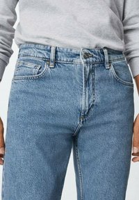 Vaqueros de mezclilla azul claro con un diseño clásico de cinco bolsillos, cierre de botones y pierna recta. La tela tiene un acabado ligeramente texturizado.