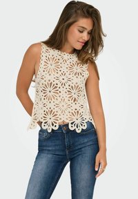 Top de ganchillo sin mangas en color crema con patrones florales, dobladillo con puntilla y diseño de calados. Combinado con unos vaqueros de mezclilla azul oscuro.