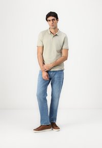 Lys grå polo skjorte, blå jeans og brune joggesko. Poloen har klassisk krage og korte ermer, med en glatt tekstur. Enkel design.