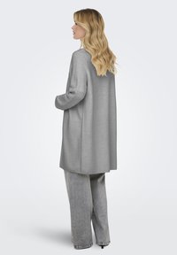 Un largo cárdigan de punto gris presenta un patrón texturizado y una silueta relajada, combinado con unos pantalones gris claro de corte holgado.