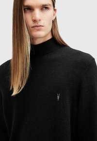Maglione nero a collo alto realizzato in tessuto morbido, con un design testurizzato e un piccolo logo ricamato sul petto.