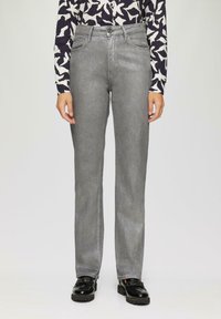 Jean en denim gris avec une coupe droite, présentant une fermeture à bouton et des passants de ceinture. Associé à une chemise à manches longues à motifs et des chaussures noires.