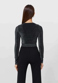 Top nero a maniche lunghe con una texture luccicante, forma aderente e scollatura rotonda; abbinato a pantaloni neri a vita alta.
