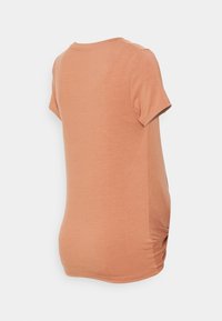 T-shirt de manga curta, cor pêssego, feito de um tecido suave, com um decote arredondado e detalhe franzido dos lados para um ajuste justo.