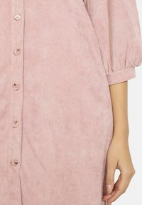 Abito in corduroy rosa polveroso con bottoni sul davanti, maniche a palloncino e una texture morbida, caratterizzato da sottili linee verticali.