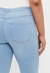 Svijetloplave traperice s prilagođenim dizajnom, s jednim stražnjim džepom i suptilno teksturiranom završnom obradom. Nema vidljivih oštećenja.