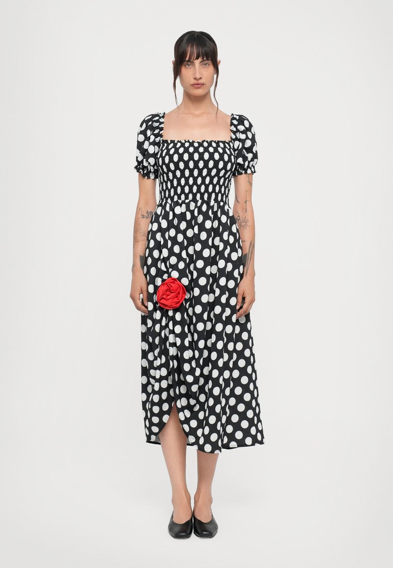 Rochie cu buline alb-negru, cu decolteu pătrat, mâneci bufante și o accente cu floare roșie. Lungime midi, material neted, fante laterale.