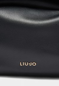 Sac en cuir noir avec une finition texturée et un logo doré métallique "LIU•JO" à l'avant, présentant un design doux et flexible.