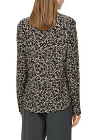 Zwarte blouse met lange mouwen en een bloemenpatroon in crèmekleuren. Heeft een afgeronde zoom en een gladde textuur. Achteraanzicht weergegeven.