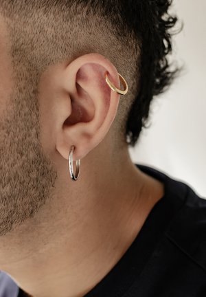 Silberner Creolenohrring und goldener runder Knorpelohrschmuck, die im Ohr getragen werden und glatte metallische Texturen sowie kontrastierende Farben zeigen.