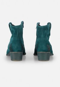 Türkise Wildleder-Stiefeletten mit runder Zehenpartie, gestapeltem Absatz, dekorativer Naht und einem Reißverschluss auf der Rückseite für ein einfaches Anziehen. Glatte Textur, minimalistische Gestaltung.