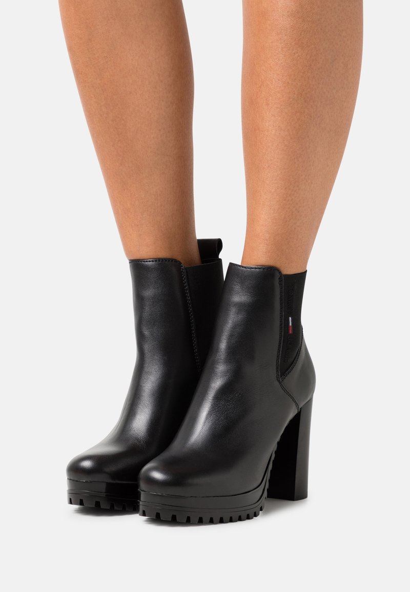 Czarne skórzane botki za kostkę na masywnym obcasie, z elastycznym bokiem i teksturowaną gumową podeszwą. Gładkie wykończenie z minimalnymi detalami akcentującymi.